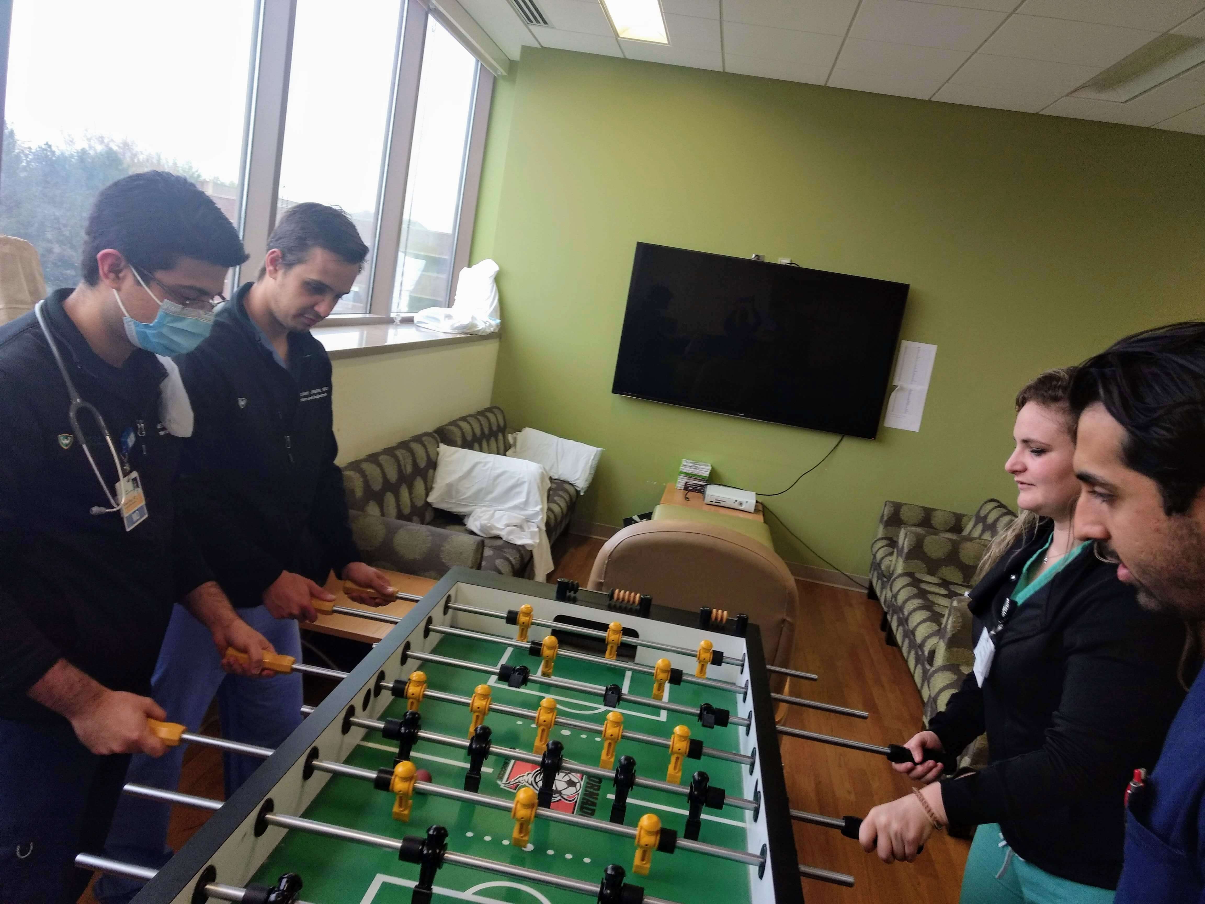 4 residents, 1 wearing a mask playing foosball together